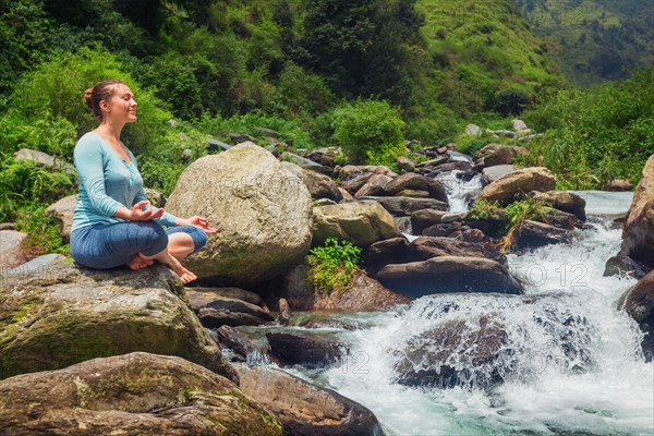 Woman doing yoga meditation asana Padmasana lotus pose outdoors at tropical waterfall