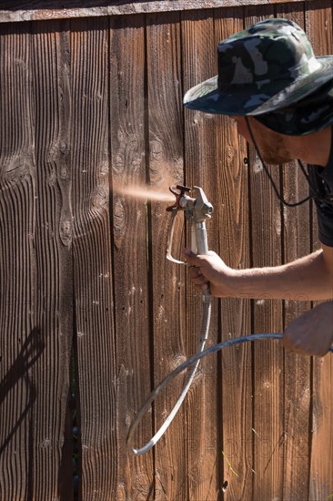 Professional painter spraying house yard fence with wood stain