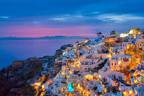 Famous greek iconic selfie spot tourist destination Oia village with traditional white houses and windmills in Santorini island in the evening blue hour