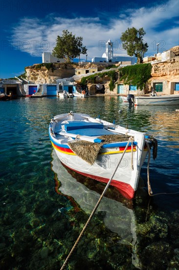 Fishing boats moored in crystal clear turquoise sea water in harbour in Greek fishing village of Mandrakia