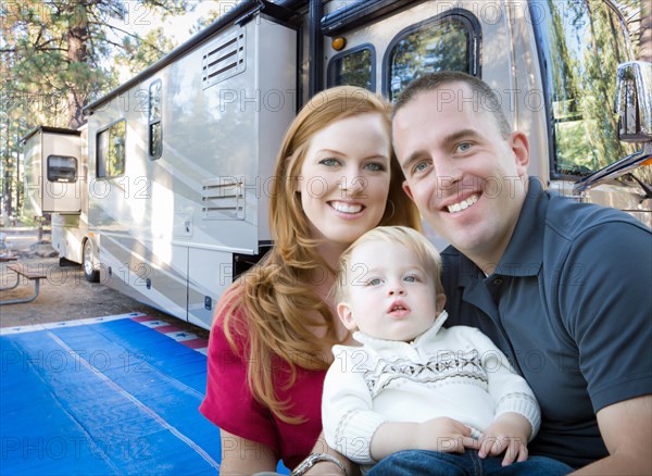 Happy young military family in front of their beautiful RV at the campground