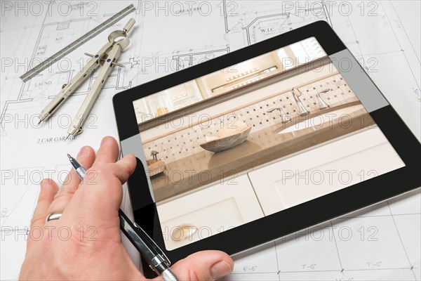 Hand of architect on computer tablet showing luxury bathroom details over house plans