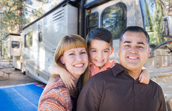 Happy young mixed-race family in front of their beautiful RV at the campground