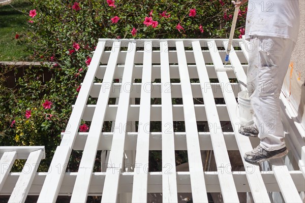 Professional painter rolling white paint onto the top of A home patio cover