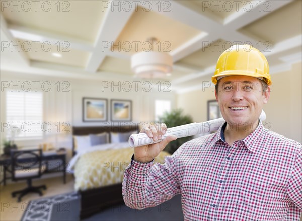 Smiling contractor in hard hat with roll of plans over custom bedroom drawing and photo combination