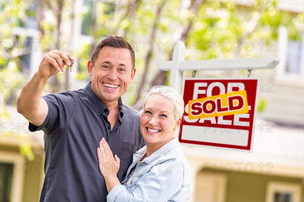 Caucasian couple in front of sold real estate sign and house with keys