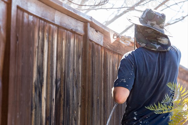 Professional painter spraying house yard fence with wood stain