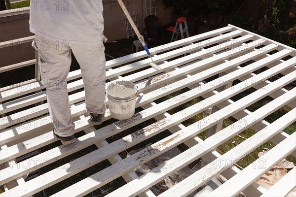 Professional painter rolling white paint onto the top of A home patio cover