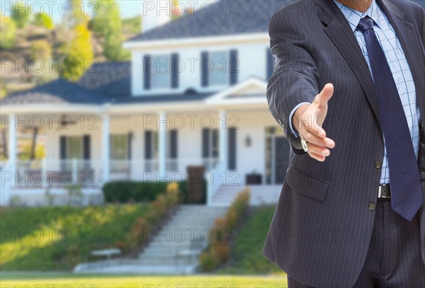 Male agent reaching for hand shake in front of beautiful new house