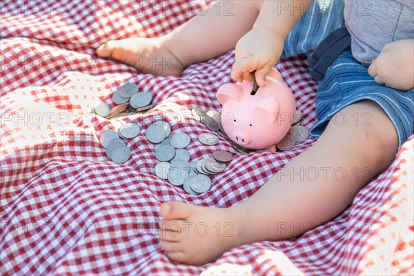 Baby boy sitting on picnic blanket putting coins in piggy bank