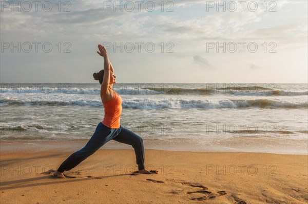 Woman doing Hatha yoga asana Virabhadrasana 1 Warrior Pose outdoors on ocean beach on sunset. Kerala