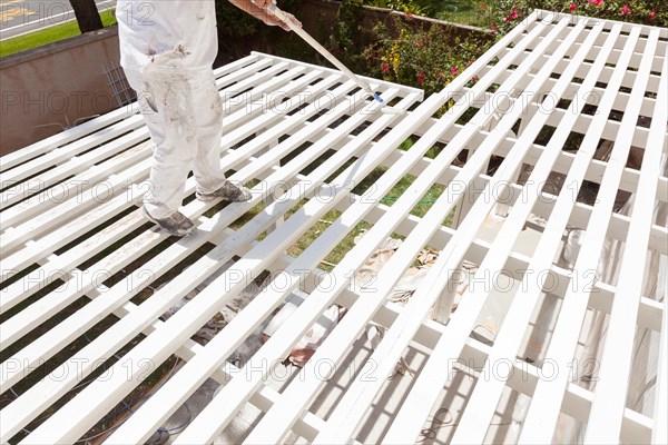 Professional painter rolling white paint onto the top of A home patio cover