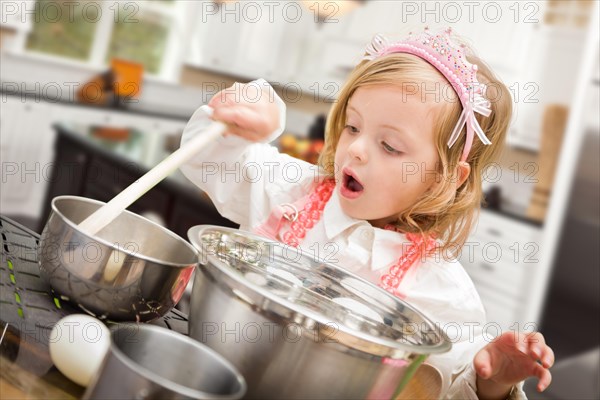 Cute baby girl playing cook with pots and pans in kitchen