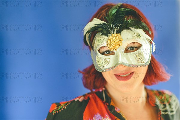 Portrait of a caucasian red head adult woman wearing a venetian theater mask
