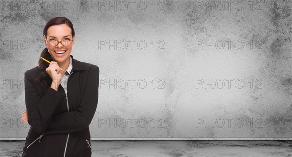 Young adult woman with pencil and glasses standing in front of blank grungy blank wall with copy space