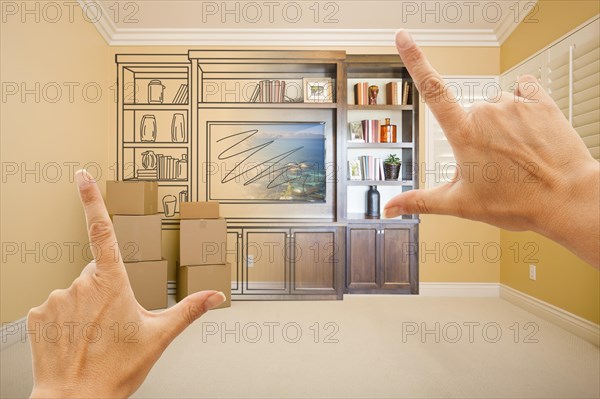 Hands framing drawing of entertainment unit gradating into photograph in room with moving boxes