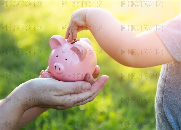 Woman holds piggy bank while baby boy puts coins inside