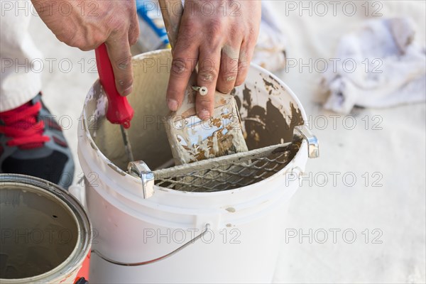 Professional painter loading paint onto his brush from A bucket