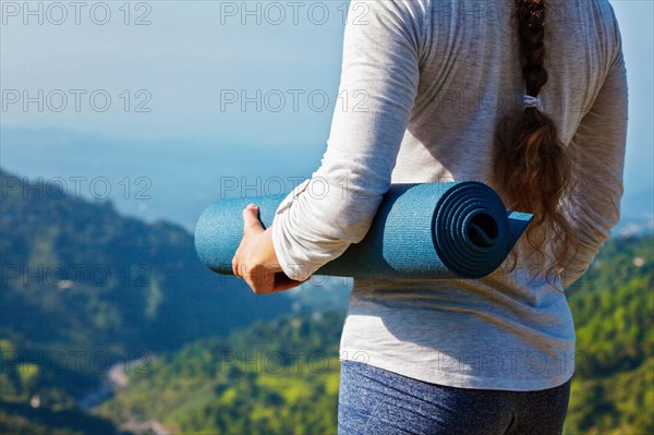 Woman standing with yoga mat outdoors in mountains close up with copyspace getting ready for yoga exercise