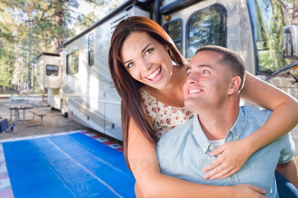 Happy caucasian couple in front of their beautiful RV at the campground