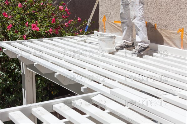 Professional painter rolling white paint onto the top of A home patio cover