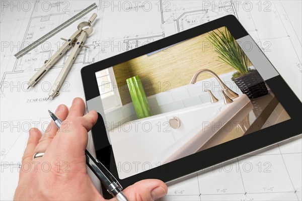 Hand of architect on computer tablet showing luxury bathroom details over house plans