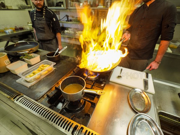 Chef cooking flambleing atlantic squid with olive oil in a big pan in a professional kitchen