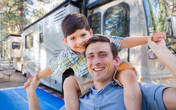 Happy young caucasian father and son in front of their beautiful RV at the campground