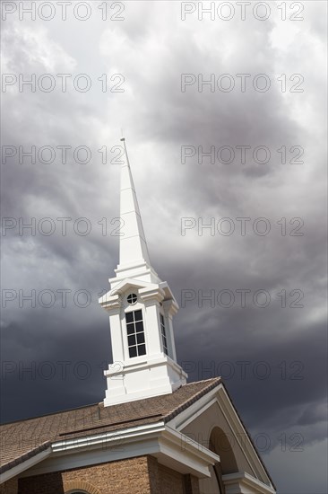Church steeple tower below ominous stormy thunderstorm clouds