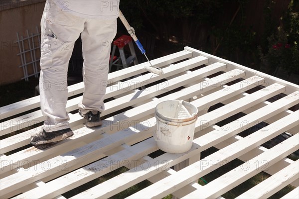 Professional painter rolling white paint onto the top of A home patio cover