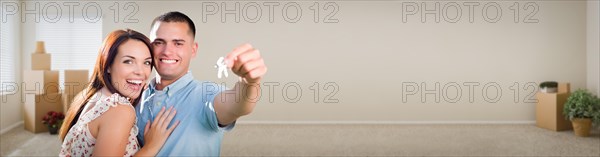 Young adult couple inside room with boxes holding new house keys banner