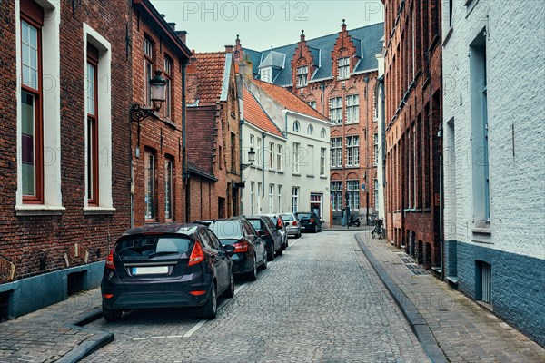 Old town Brugge street with cobblestone road with parked cars and old medieval houses