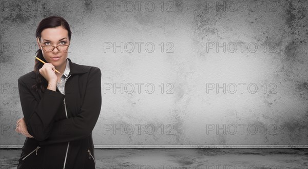 Young adult woman with pencil and glasses standing in front of blank grungy blank wall with copy space