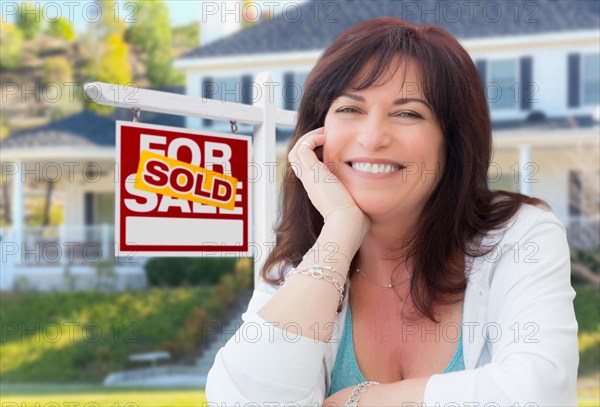 Middle aged woman in front of house with sold for sale real estate sign in yard