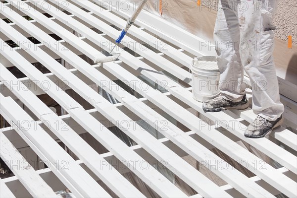 Professional painter rolling white paint onto the top of A home patio cover