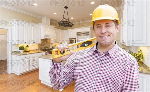 Smiling contractor with level wearing hard hat standing in custom kitchen