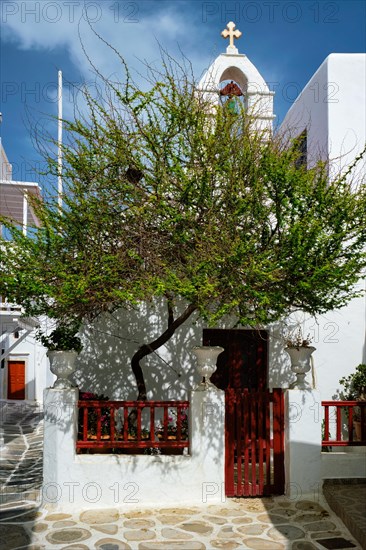 Picturesque scenic narrow Greek streets with traditional whitewashed houses with blue doors windows of Mykonos town and orthodox church in famous tourist attraction Mykonos island