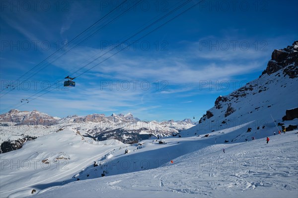 View of a ski resort piste with people skiing in Dolomites in Italy with cable car ski lift. Ski area Arabba. Arabba