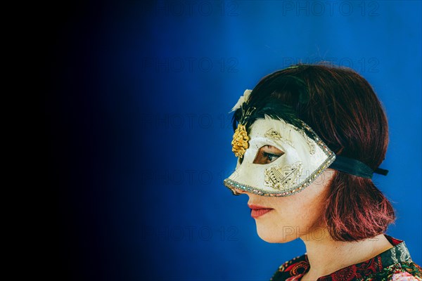 Portrait of a caucasian red head adult woman wearing a venetian theater mask