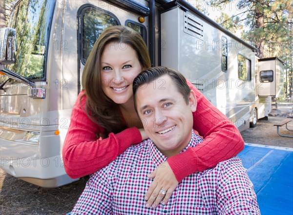 Happy caucasian couple in front of their beautiful RV at the campground