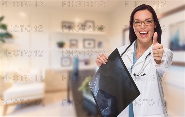 Young female doctor or nurse with thumbs up standing in office holding x-ray