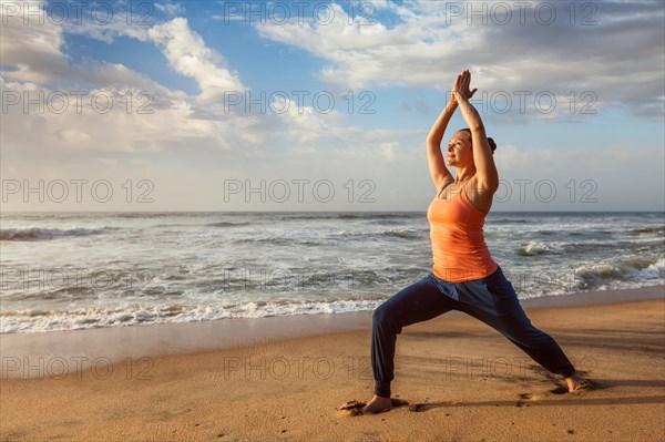 Woman doing Hatha yoga asana Virabhadrasana 1 Warrior Pose outdoors on ocean beach on sunset. Kerala
