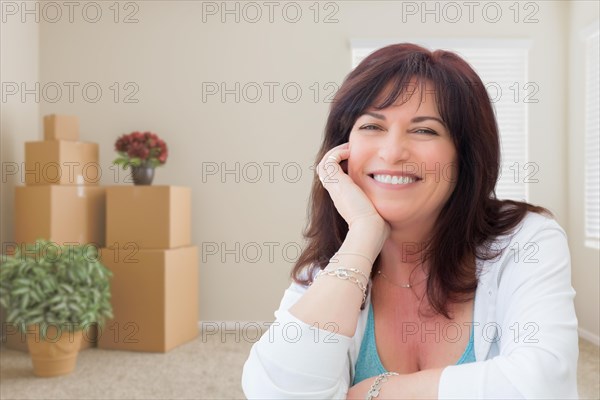 Middle aged woman relaxing inside empty room with moving boxes