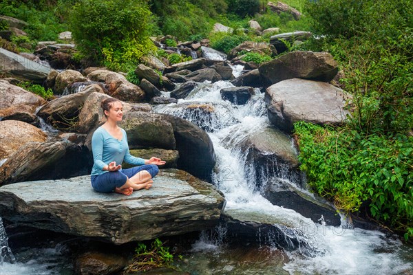 Woman doing yoga meditation asana Padmasana lotus pose outdoors at tropical waterfall