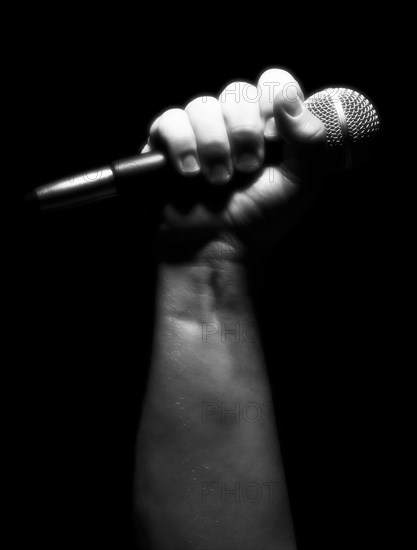 Gray scale vertical microphone clinched firmly in male fist on a black background