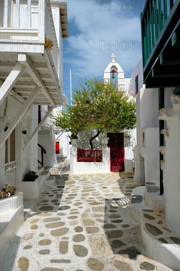 Picturesque scenic narrow Greek streets with traditional whitewashed houses with blue doors windows of Mykonos town and orthodox church in famous tourist attraction Mykonos island