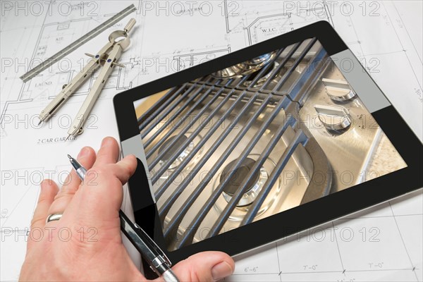 Hand of architect on computer tablet showing kitchen stove details over house plans