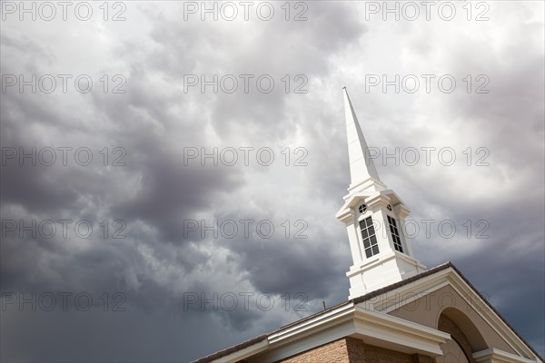 Church steeple tower below ominous stormy thunderstorm clouds