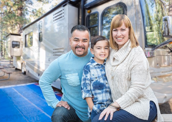 Happy young mixed-race family in front of their beautiful RV at the campground