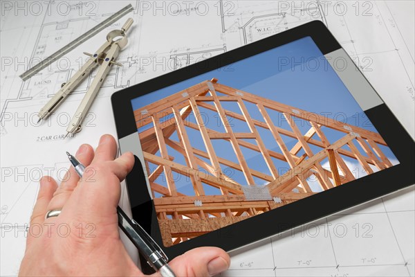 Hand of architect on computer tablet showing home framing photo over house plans